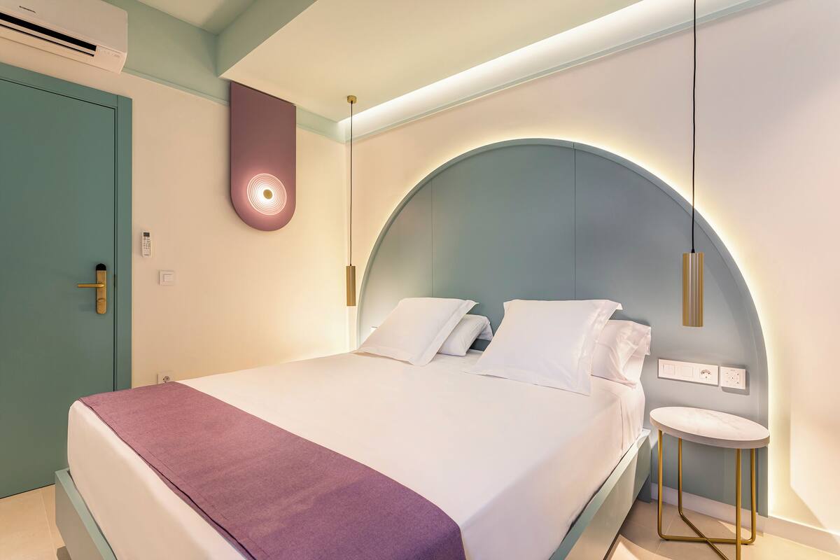 Un dormitorio moderno con cama, mesita de noche y lámpara de pared.
