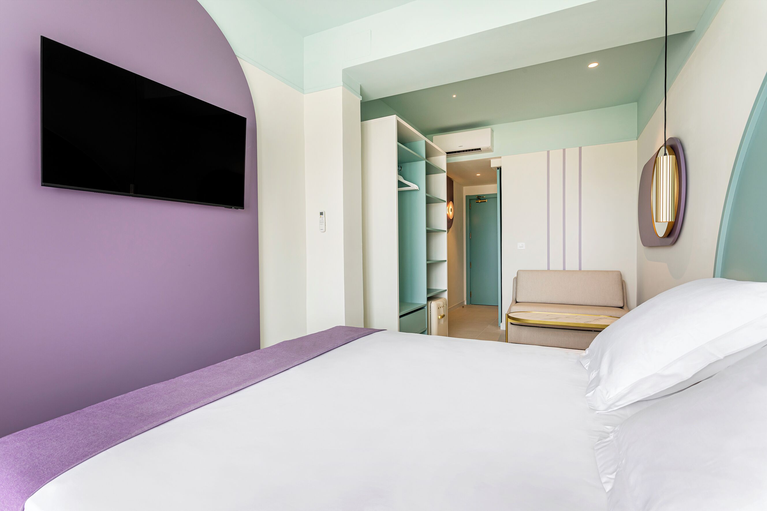 Una habitación de hotel moderna con cama, televisor montado en la pared, vestidor y una lámpara colgante.