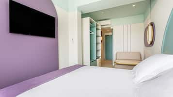Una habitación de hotel moderna con cama, televisor montado en la pared, vestidor y una lámpara colgante.