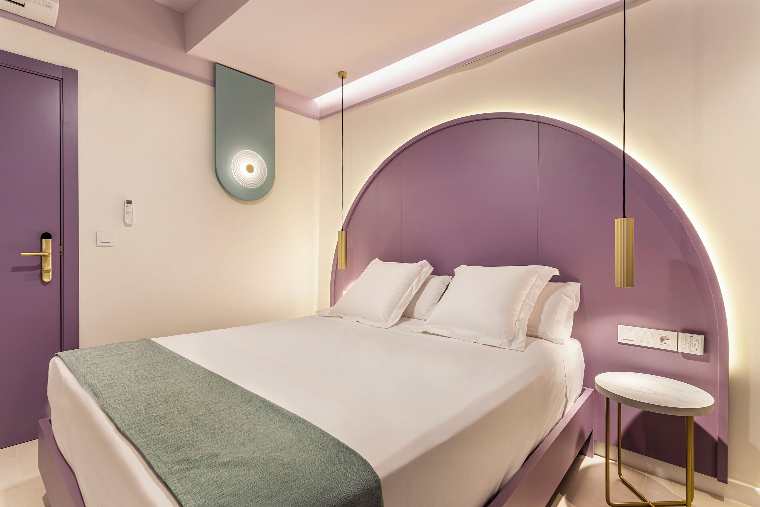 Un dormitorio moderno con cama, mesita de noche y un original cabecero morado.
