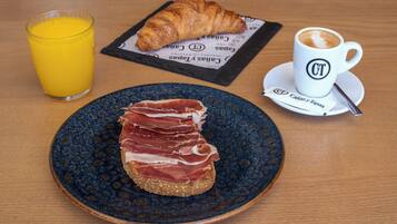 Un desayuno con un croissant, un vaso de zumo de naranja y una taza de café sobre una mesa de madera.
