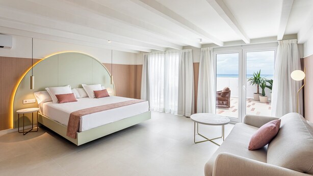 A modern hotel room with a bed, a sofa, a round coffee table, and a balcony with a view. - Blue Malva (Valencia)