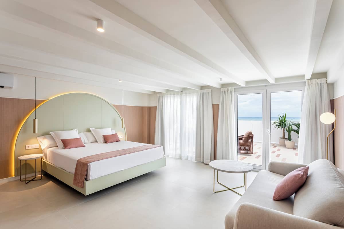 Una habitación de hotel moderna con cama, sofá, una mesita redonda y un balcón con vistas.