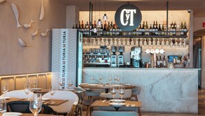 A restaurant interior with tables set for dining, a bar area with a variety of bottles and glasses, and a sign with the initials 'CT'. - Blue Malva (Valencia)