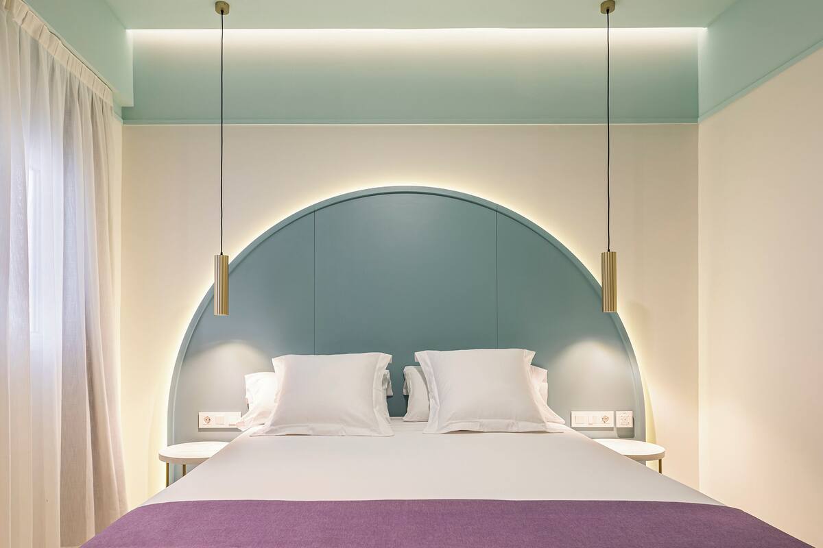Una habitación de hotel moderna con una cama grande, dos mesitas de noche y un diseño de techo abovedado único.