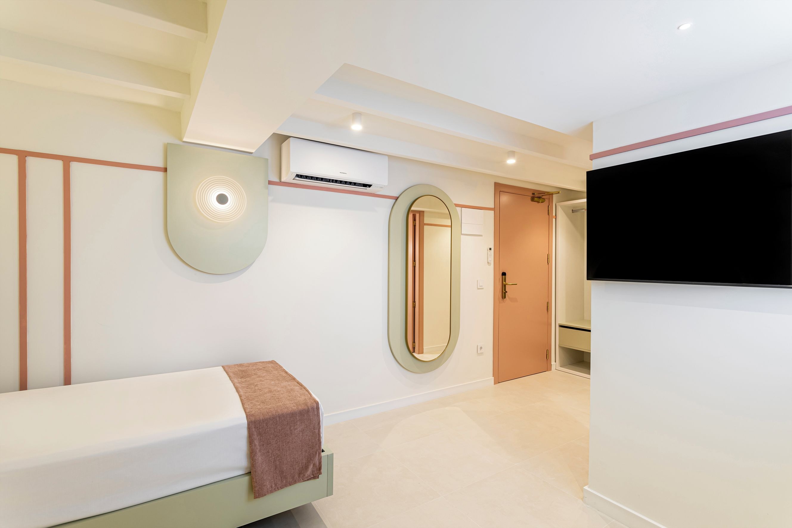 Una habitación de hotel moderna con una cama, aire acondicionado de pared, un espejo grande y un televisor.