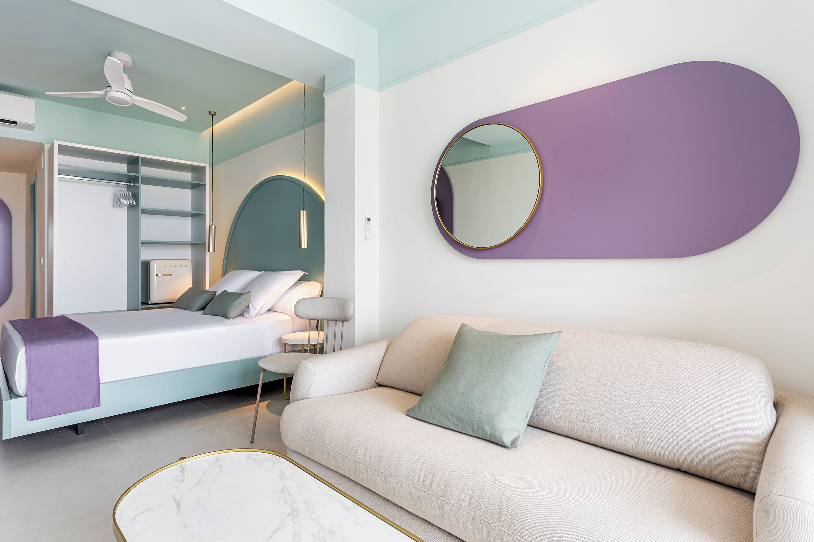 A modern bedroom with a bed, a sofa, a round mirror, and a ceiling fan.