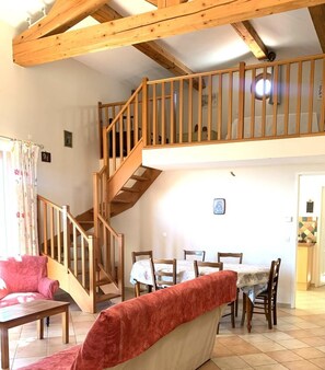 Ein großzügiger Wohnbereich mit einer Holztreppe zu einer oberen Etage, einem Esstisch mit Stühlen und einem roten Sofa.