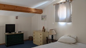 Un dormitorio con cama, cómoda, televisor, lámpara y ventana con cortina.