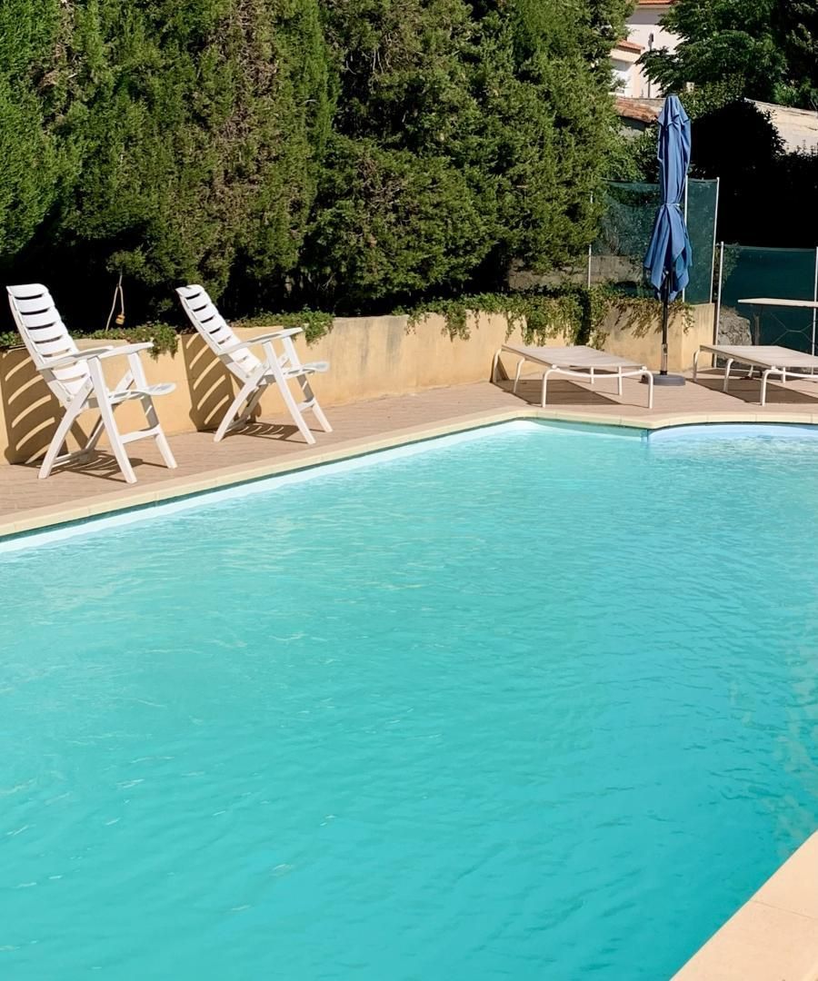 A swimming pool with white lounge chairs and a sun umbrella.