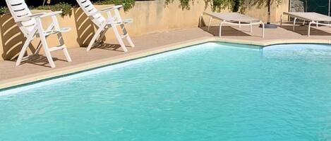 A swimming pool with white lounge chairs and a sun umbrella.