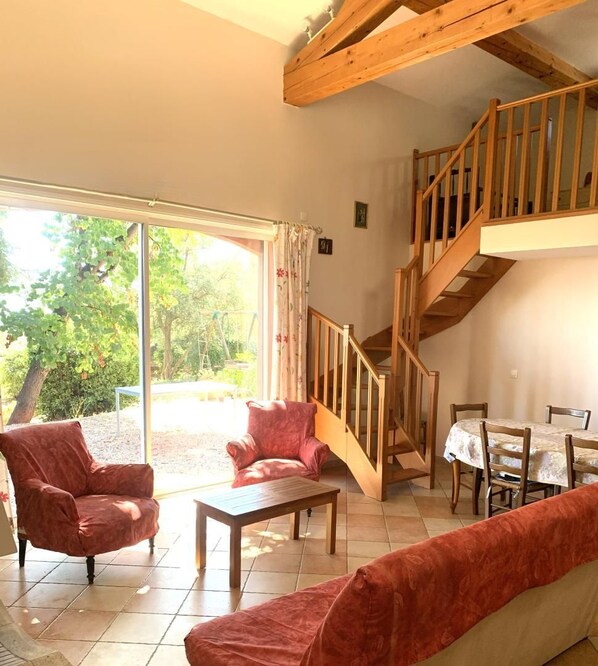 A living room with a staircase, a sofa, a table, and a view of the outdoors.