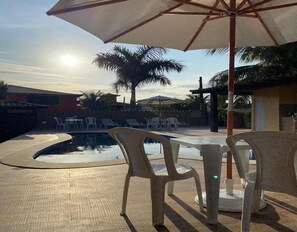Un área junto a la piscina con una piscina pequeña, sillas de plástico blancas y un paraguas grande.