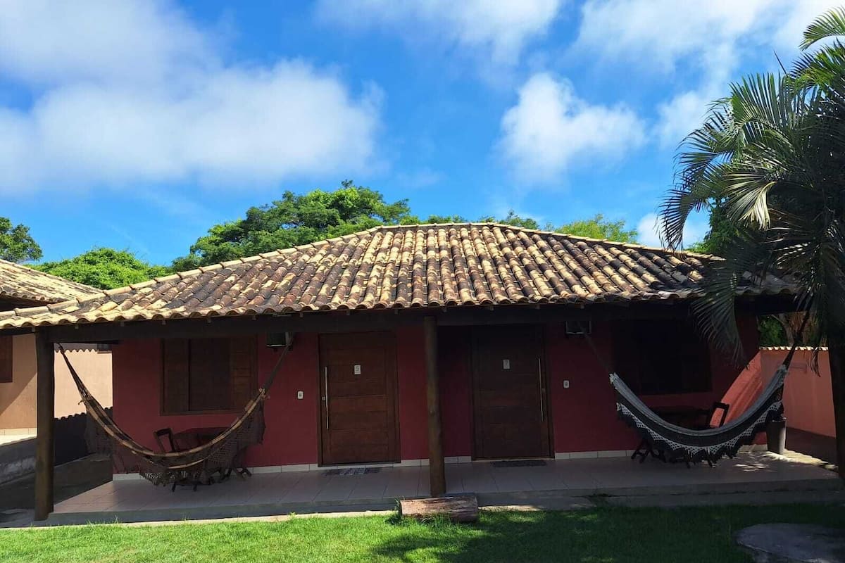 Un bâtiment rouge avec un toit en tuiles, deux hamacs et une pelouse verdoyante.