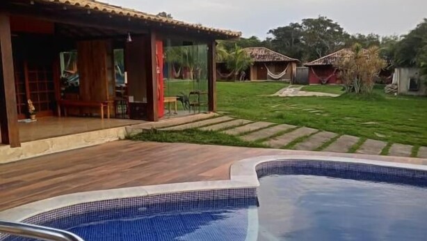 Piscina com duas cadeiras de metal, um deck de madeira e uma área coberta com um banco.
