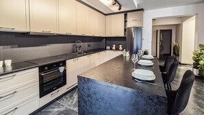 A modern kitchen with a large island, black countertops, and white cabinetry. There are two sinks, a stove, and a refrigerator.