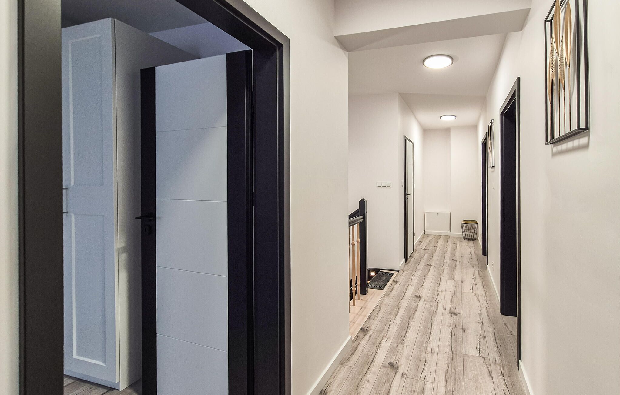 A hallway with a wooden floor, white walls, and black-framed doors.