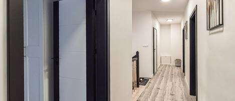 A hallway with a wooden floor, white walls, and black-framed doors.
