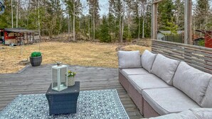 A deck with a sofa and a patterned rug, surrounded by a forested area. - Lovely home in Norrtälje with sauna (Norrtälje)