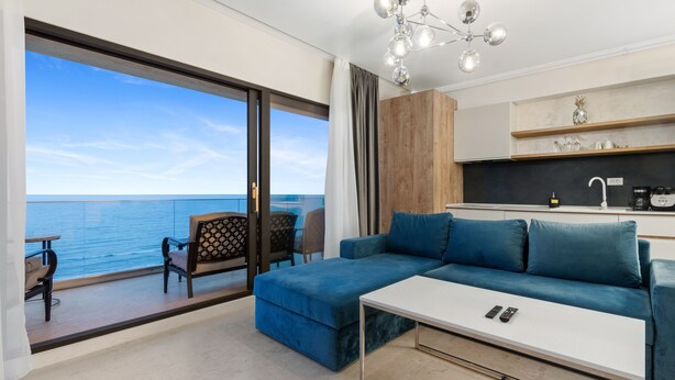 A modern living room with a blue sectional sofa, a white coffee table, and a view of the ocean through large sliding doors. - Gioia Sea View (Navodari)