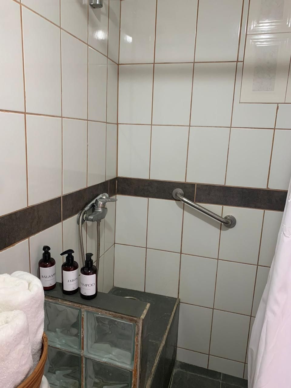 Een badkamer met witte en bruine tegels, een douchecabine van glas en drie flessen toiletartikelen op een plank.