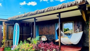 A beach house with a thatched roof, a surfboard leaning against the wall, and a hammock on the porch. - Paraíso Sunset Bungalows (Hanga Roa)