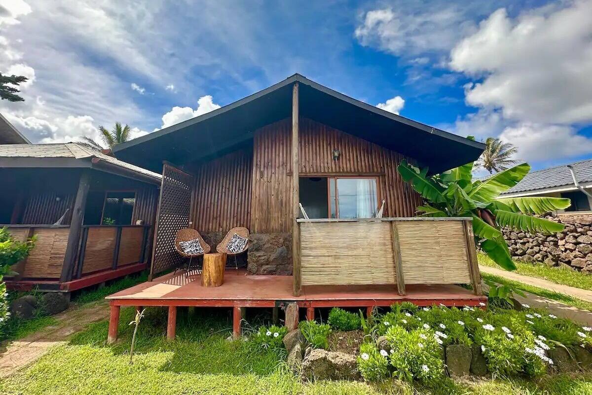A rustic wooden house with a porch, two chairs, and a table.
