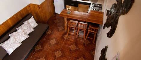 Cocina compacta con microondas, estufa y pileta. Se observa un banco de madera con un cojín y dos sillas.