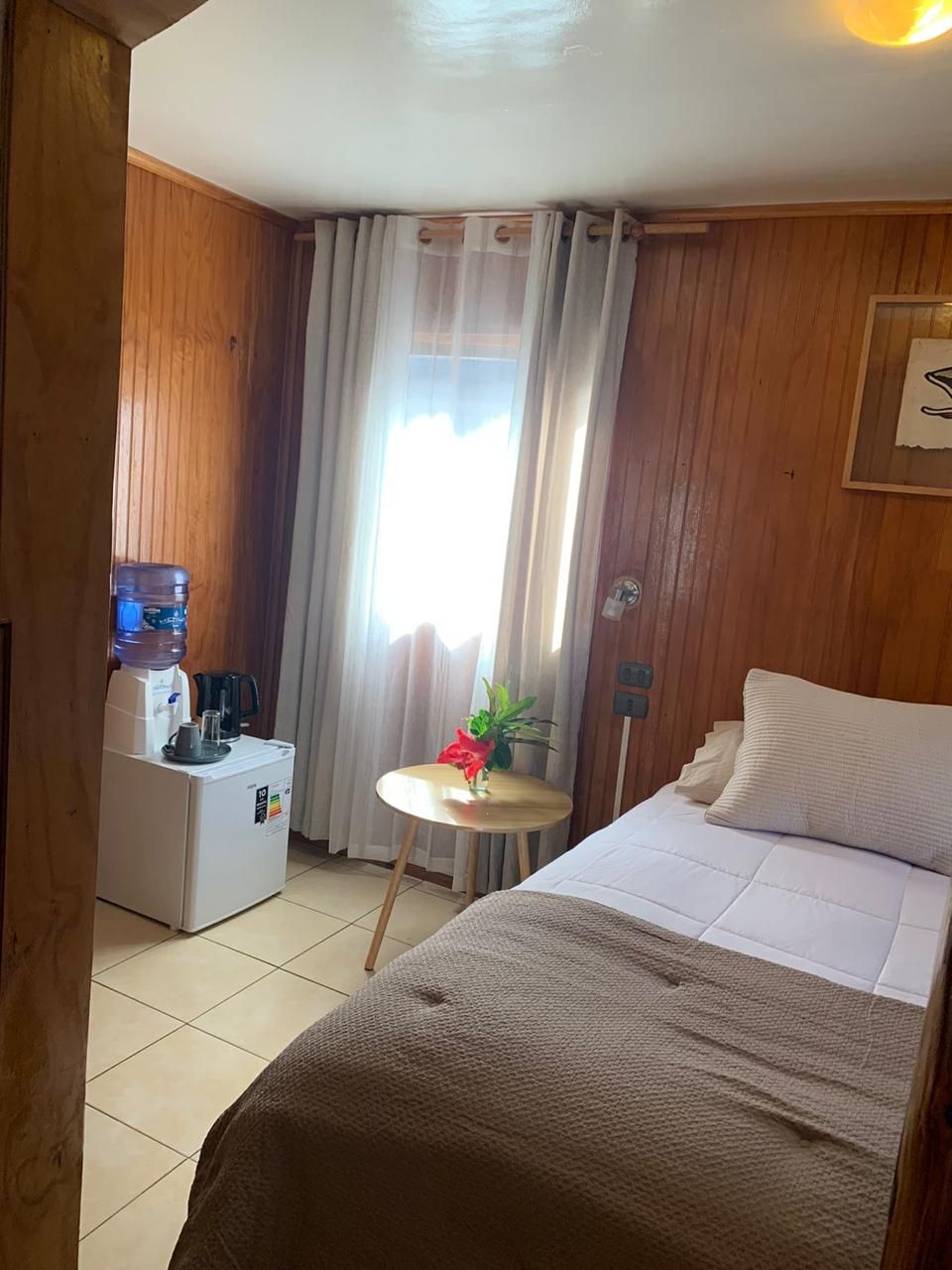 Une chambre d’hôtel avec un lit, une petite table sur laquelle est posée une plante, une machine à café et un distributeur d’eau.