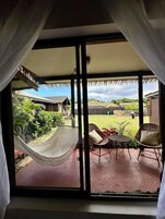 Una habitación con un amplio ventanal corredero que da a un patio exterior con una hamaca, sillas de mimbre y una pequeña mesa.