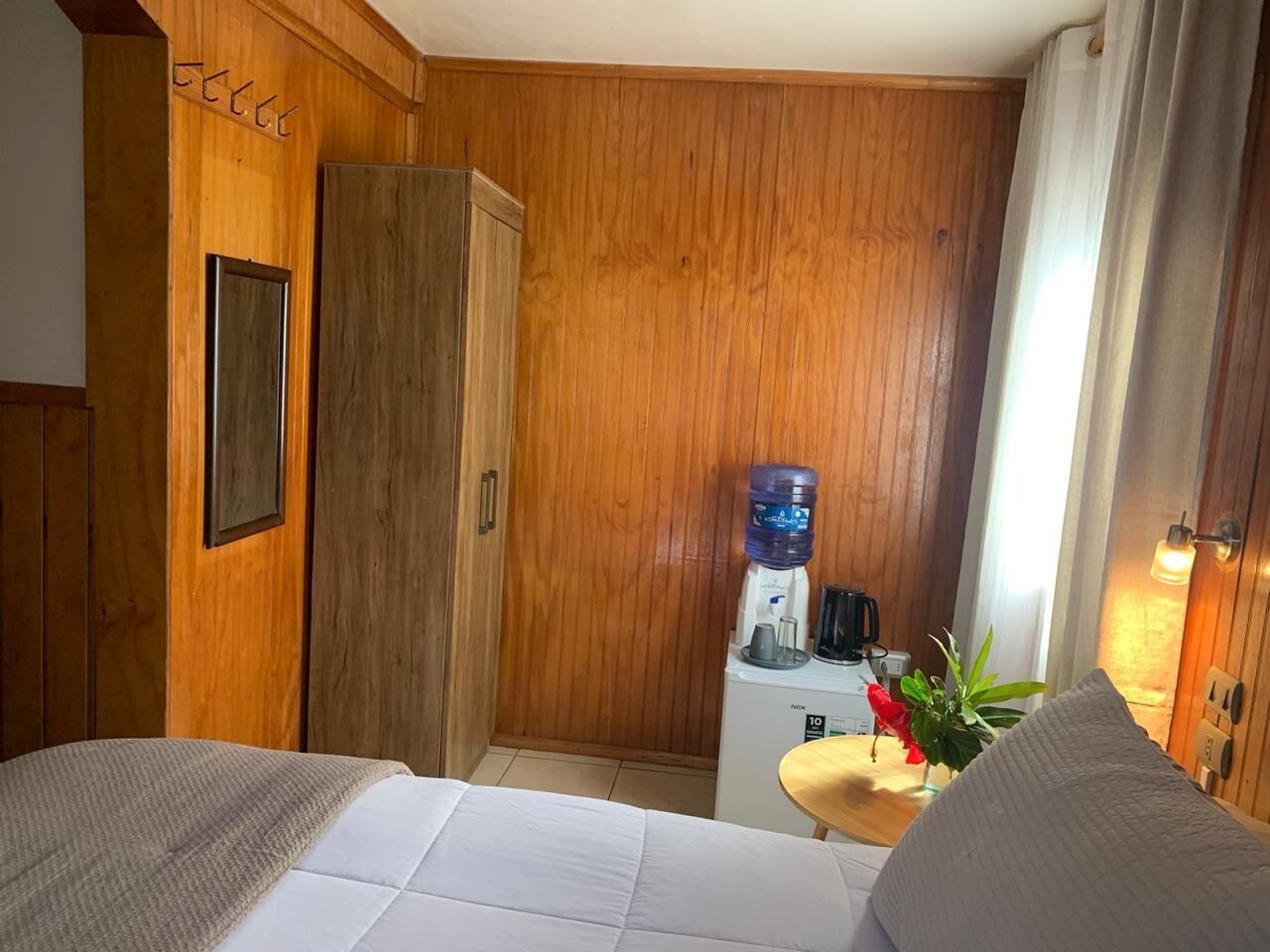 Une chambre d’hôtel avec des panneaux de bois au mur, un lit, un bureau avec un distributeur d’eau et une machine à café.
