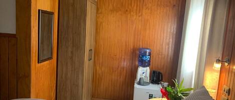 Une chambre d’hôtel avec des panneaux de bois au mur, un lit, un bureau avec un distributeur d’eau et une machine à café.