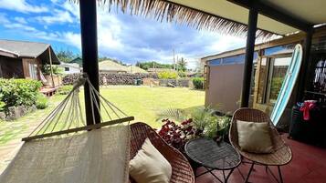 A hammock, wicker chairs, a small table, and a view of a garden and buildings.