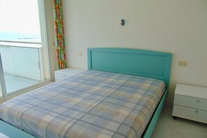 A bedroom with a bed, a nightstand, a window with curtains, and a view of the outside.