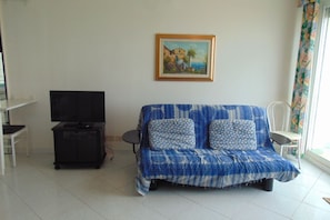 A living room with a sofa, a TV stand, a painting, and a window with curtains.
