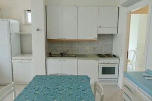 A compact kitchen with white cabinets, a countertop, a sink, a stove, and a refrigerator.