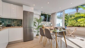 Una cocina moderna con armarios blancos, un refrigerador de acero inoxidable y un comedor con mesa y sillas de vidrio.