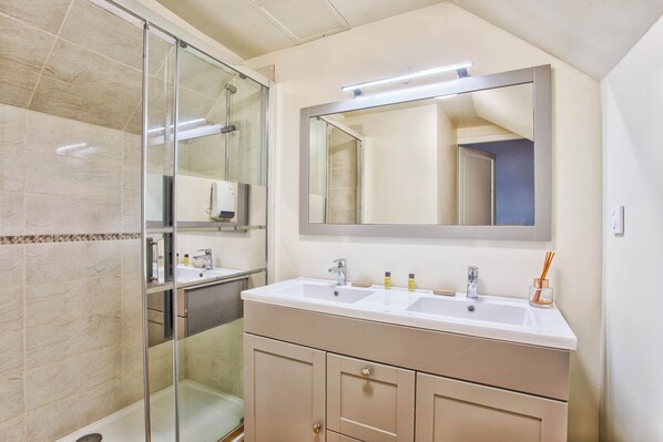 A bathroom with a glass shower enclosure, a double sink vanity, and a large mirror above the vanity.