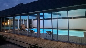 A modern building with a swimming pool, glass doors, and wooden deck. - Elegant Manor with in Normandy by the sea - 8 rooms for 22 persons. Pool and spa (SULLY)