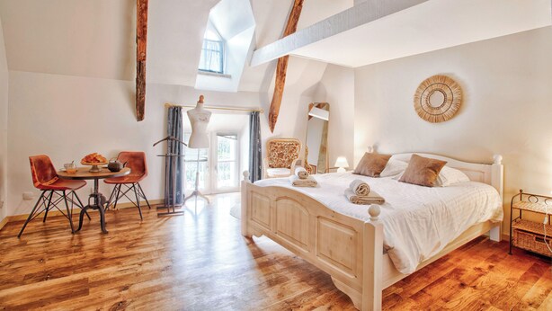 A bedroom with a wooden bed, a dining table with chairs, and a large window. - Elegant Manor with in Normandy by the sea - 8 rooms for 22 persons. Pool and spa (SULLY)