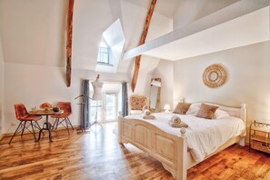 A bedroom with a wooden bed, a dining table with chairs, and a large window.