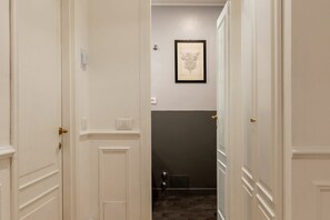 A hallway with white doors, a framed artwork on the wall, and a dark tiled floor.