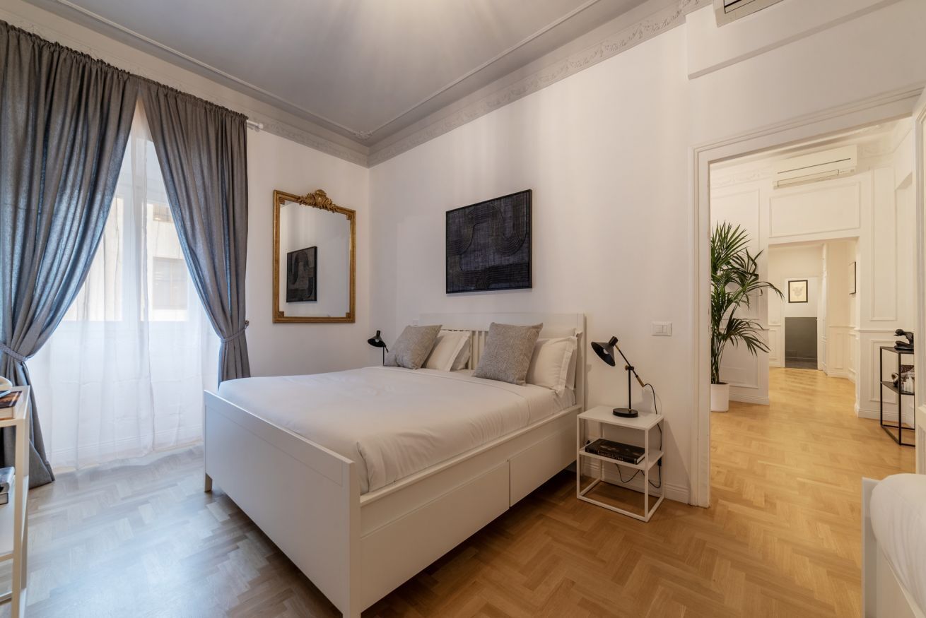 A bedroom with a large bed, a bedside table with a lamp, a mirror, and a painting on the wall.