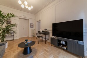 Ein modernes Wohnzimmer mit großem Flachbildfernseher, einem Essbereich mit schwarzem Tisch und Stühlen sowie einer Zimmerpflanze.