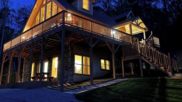 A large log cabin with a spacious deck and multiple windows, surrounded by trees. - New cabin with king size bedrooms, en suite bathrooms, smart TV, decks & views. (Fairview)