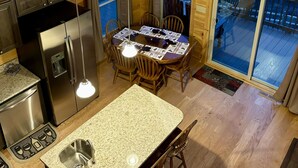 A modern kitchen with a central island, stainless steel appliances, and a dining area with a round table and chairs. - New cabin with king size bedrooms, en suite bathrooms, smart TV, decks & views. (Fairview)