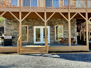 Eine zweistöckige Holzhütte mit Natursteinfassade, einer Veranda und einem Grill vor der Tür.