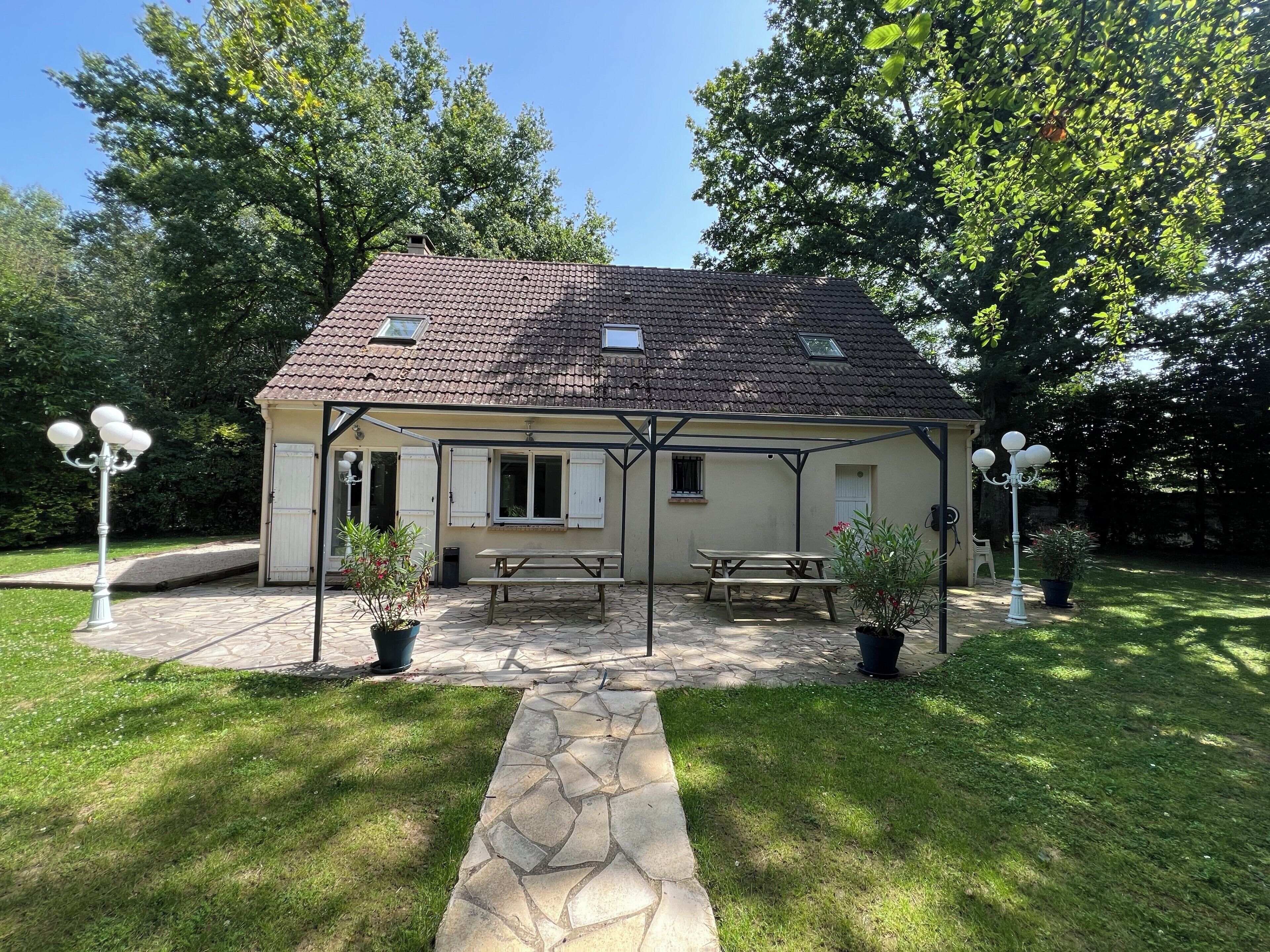 A house with a tiled roof, a covered patio with a table and benches, and two lamp posts.