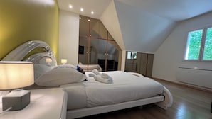 A modern bedroom with a large bed, a bedside table, a lamp, and a view of the outdoors through a window.