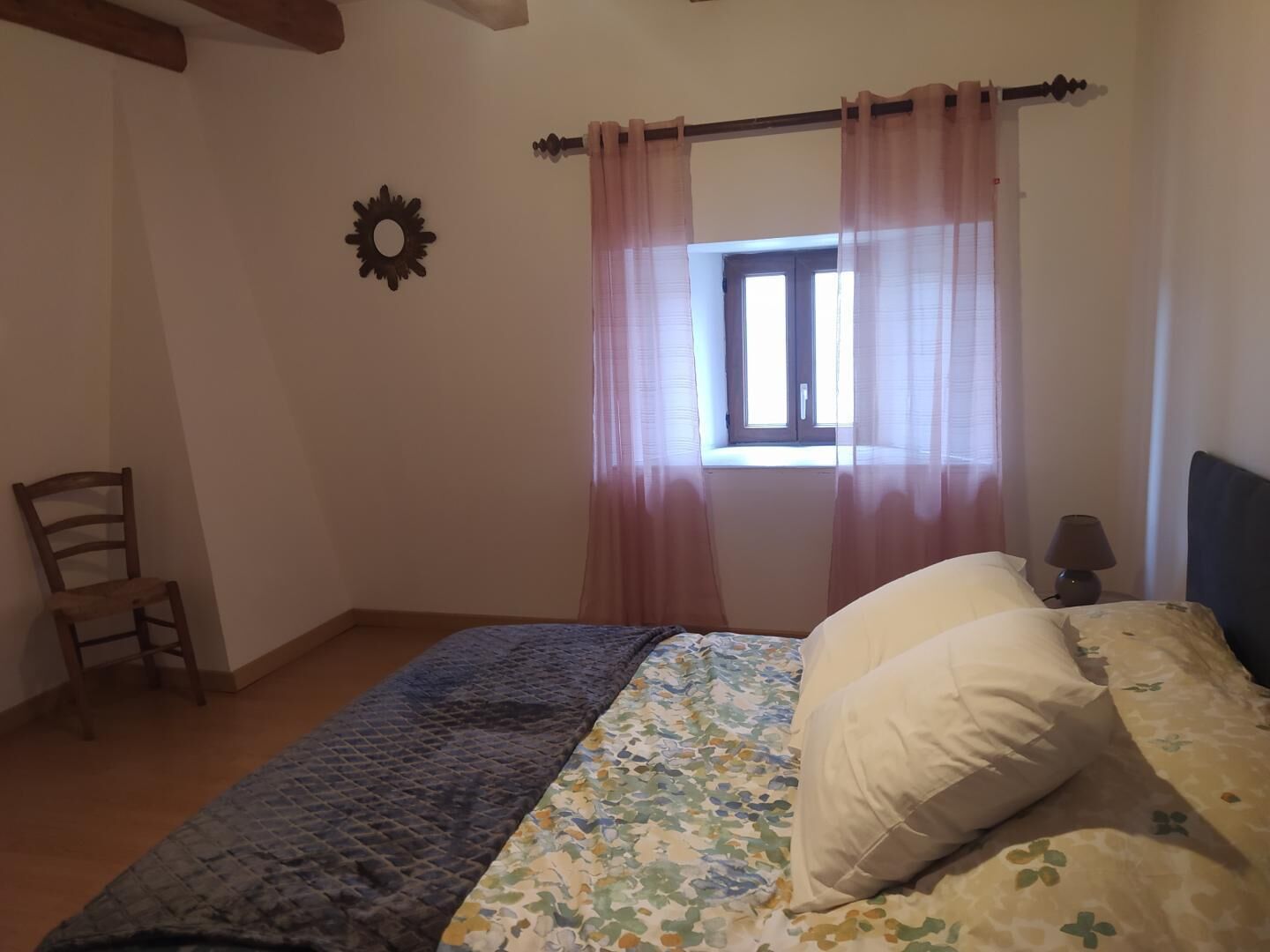 Ein Schlafzimmer mit Bett, Sessel, einem Fenster mit Vorhängen und einer Wanddekoration.